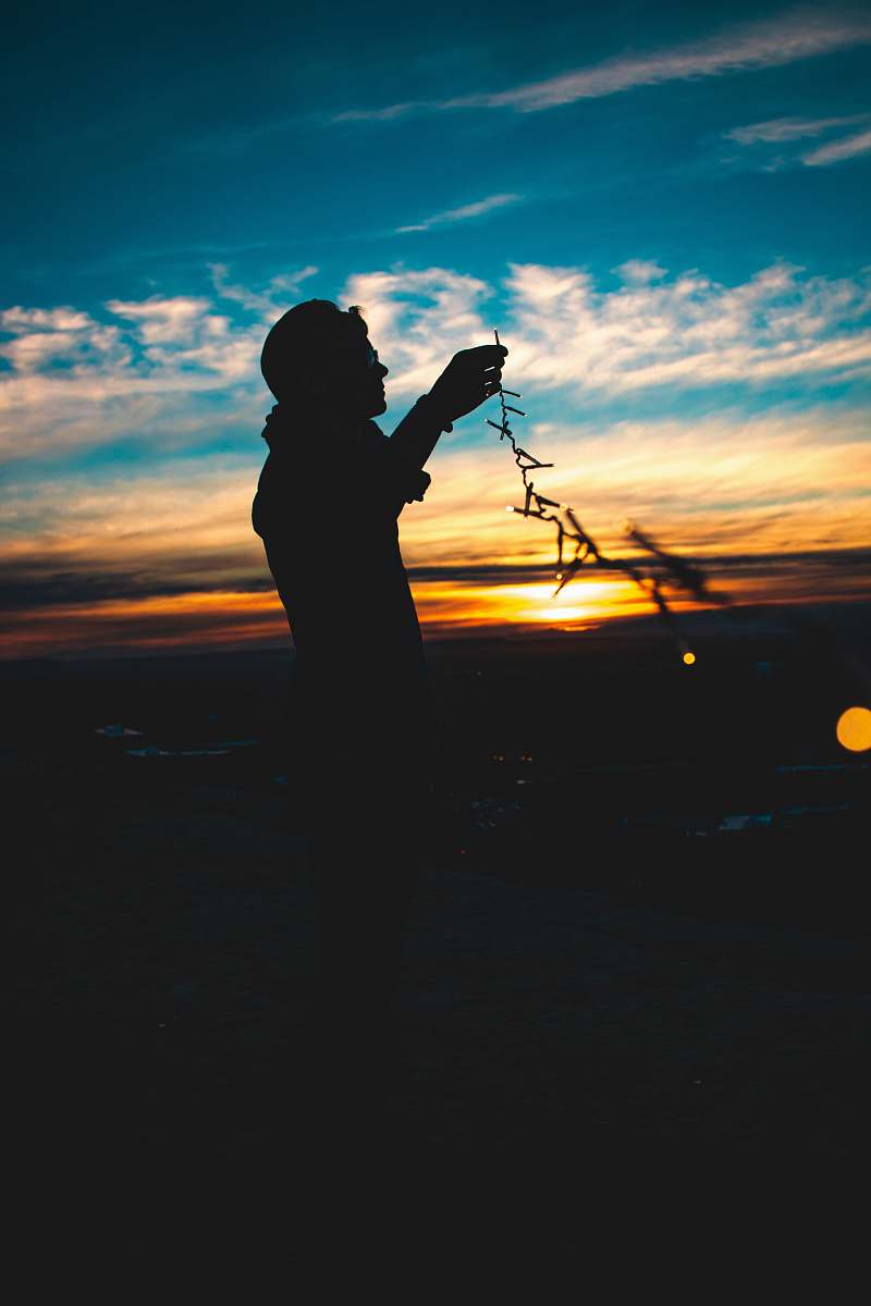 person silhouette of person holding string lights during sunset sunrise