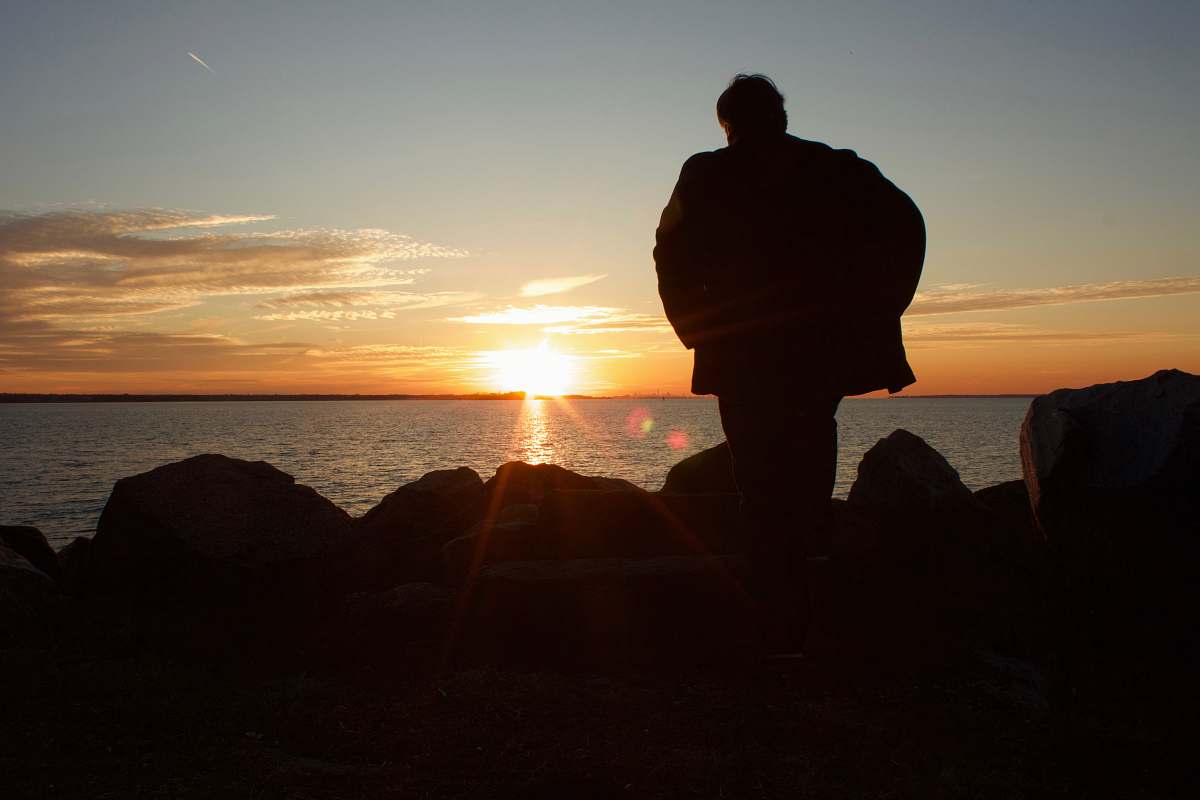 person silhouette of person in front of body of water during daytime human