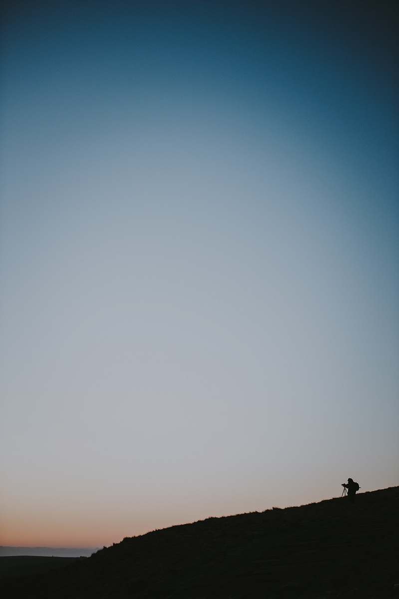 grey silhouette of person on top of a hill sky