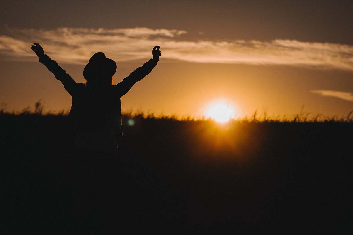 sun silhouette of person raising his two arms during sunrise sky