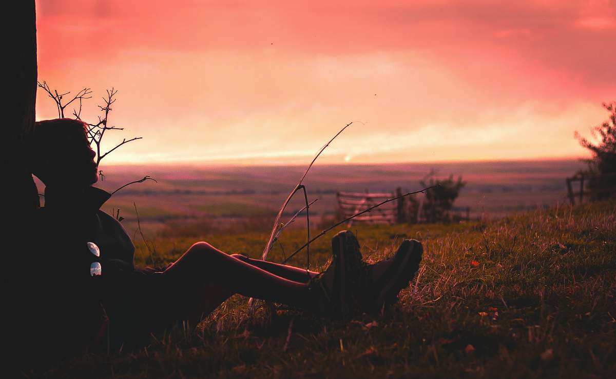 sunset silhouette of person sitting on green grass during golden hour gate