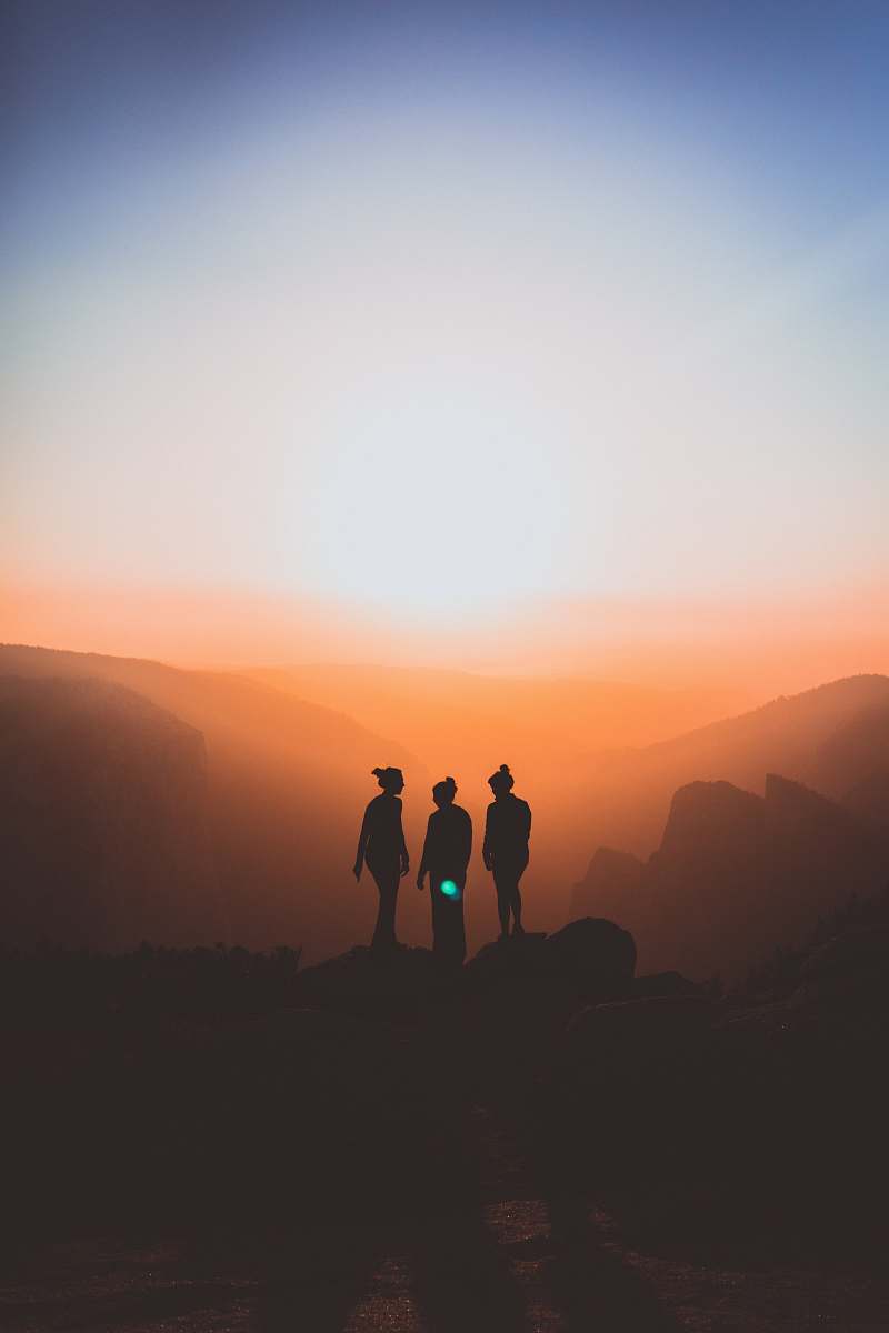 woman silhouette of three people up on mountain cliff sunset