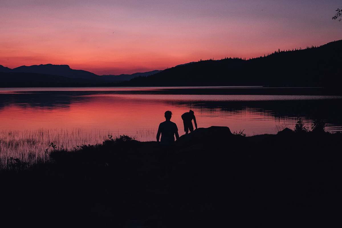 person silhouette of two people standing near body of water under orange sky nature