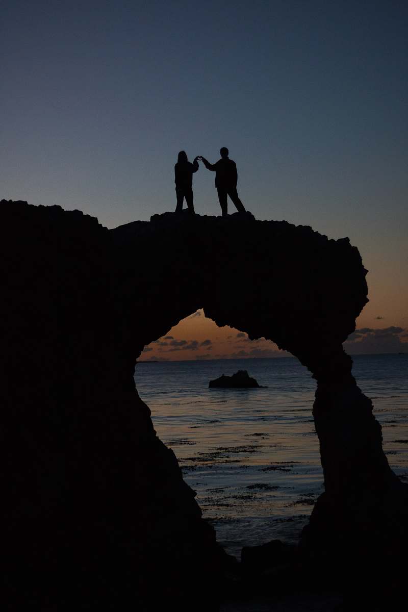 water silhouette of two persons atop a rock formation near the ocean sea