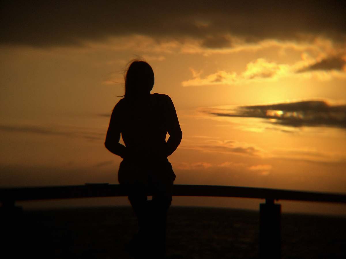 human silhouette of woman standing near beach line person