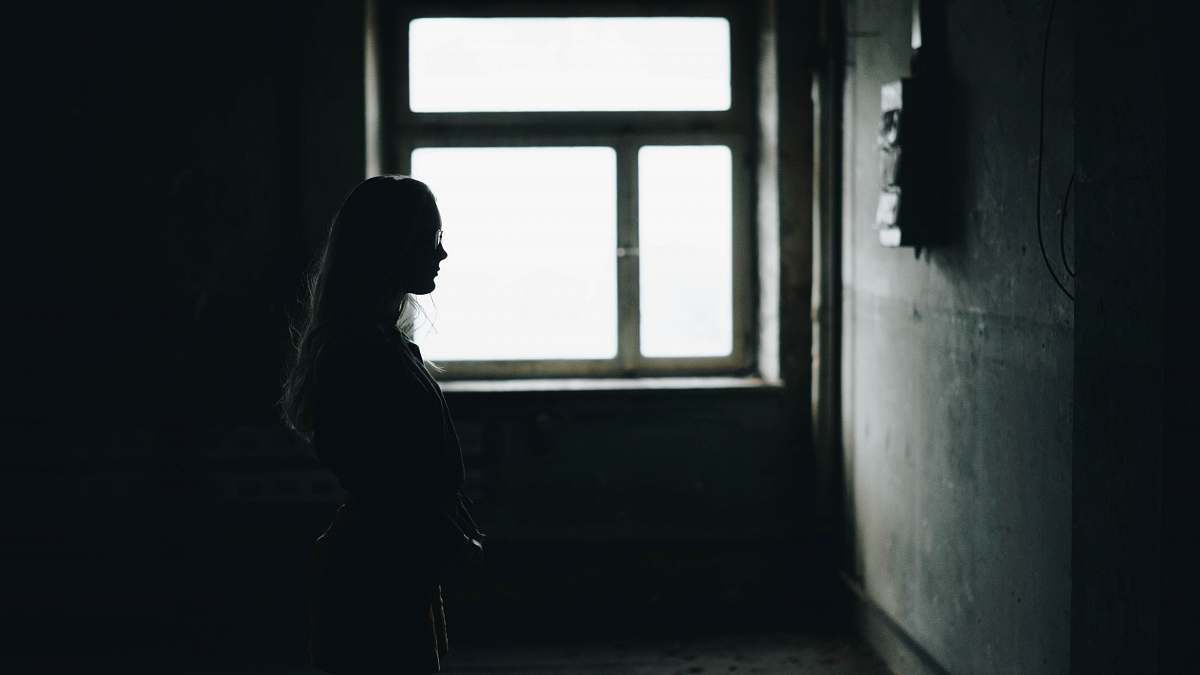 person silhouette of woman standing while facing wall inside room human