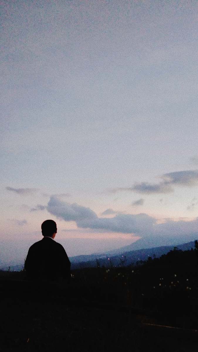 human silhouette photo of man sitting on rock formation grey