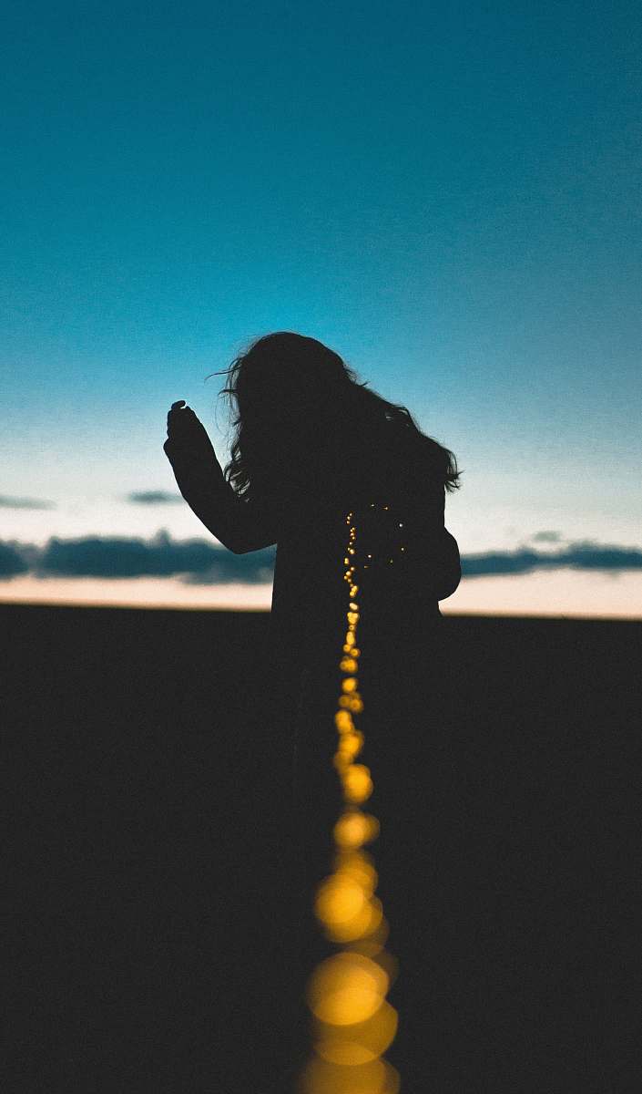 light silhouette photo of person holding string lights turned on blue