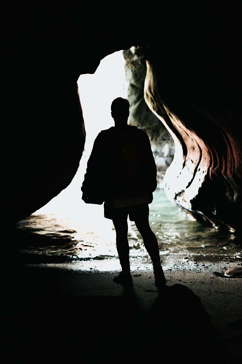person silhouette photo of person standing in front of blue body of water inside cave during daytime people