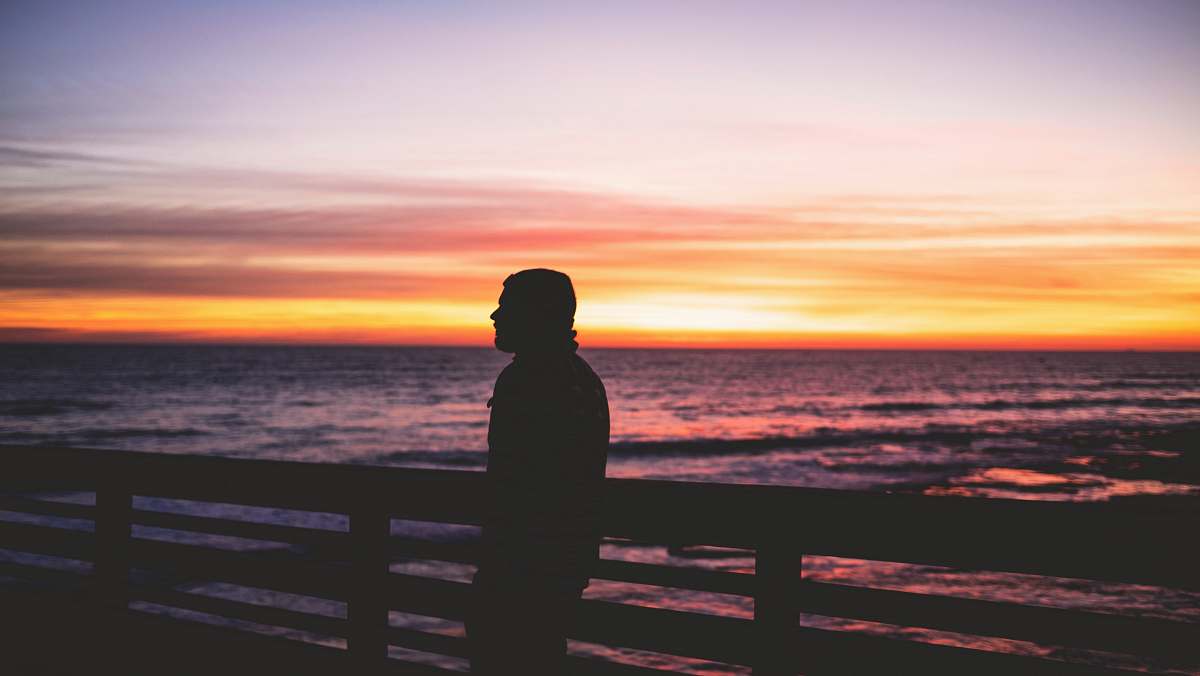 human silhouette photo of person standing near body of water person