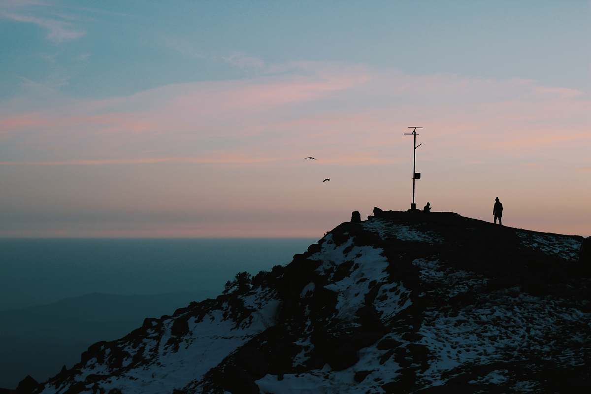 sunset silhouette photo of person standing on mountain sky