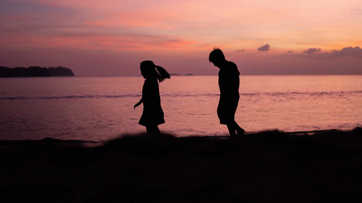 human silhouette photography of boy and girl walking beside shoreline person