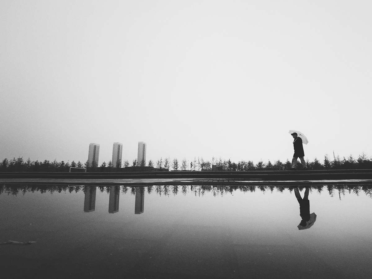 human silhouette photography of man holding umbrella beside body of water black-and-white
