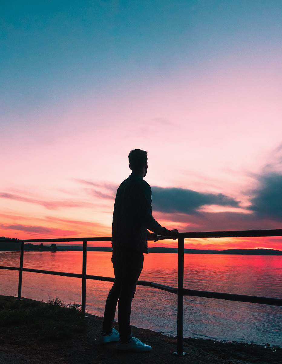 human silhouette photography of man leaning against metal fence railing