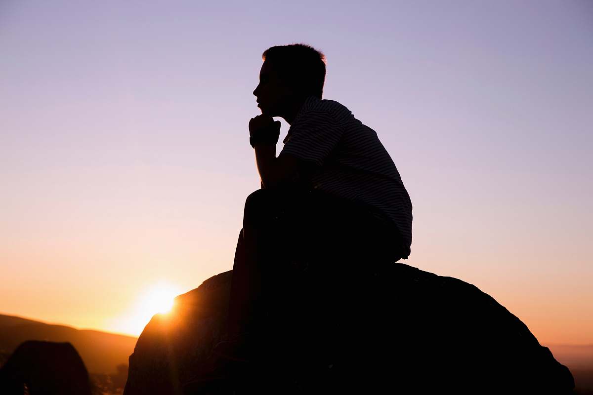person silhouette photography of man sitting on stone human