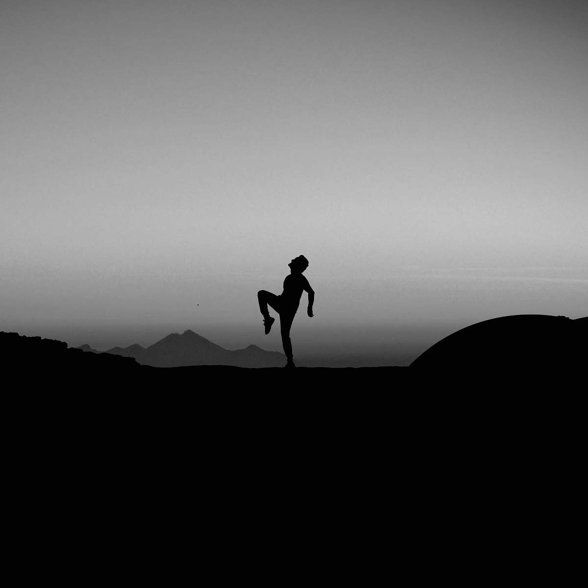 black-and-white silhouette photography of man standing with one leg on ground grey