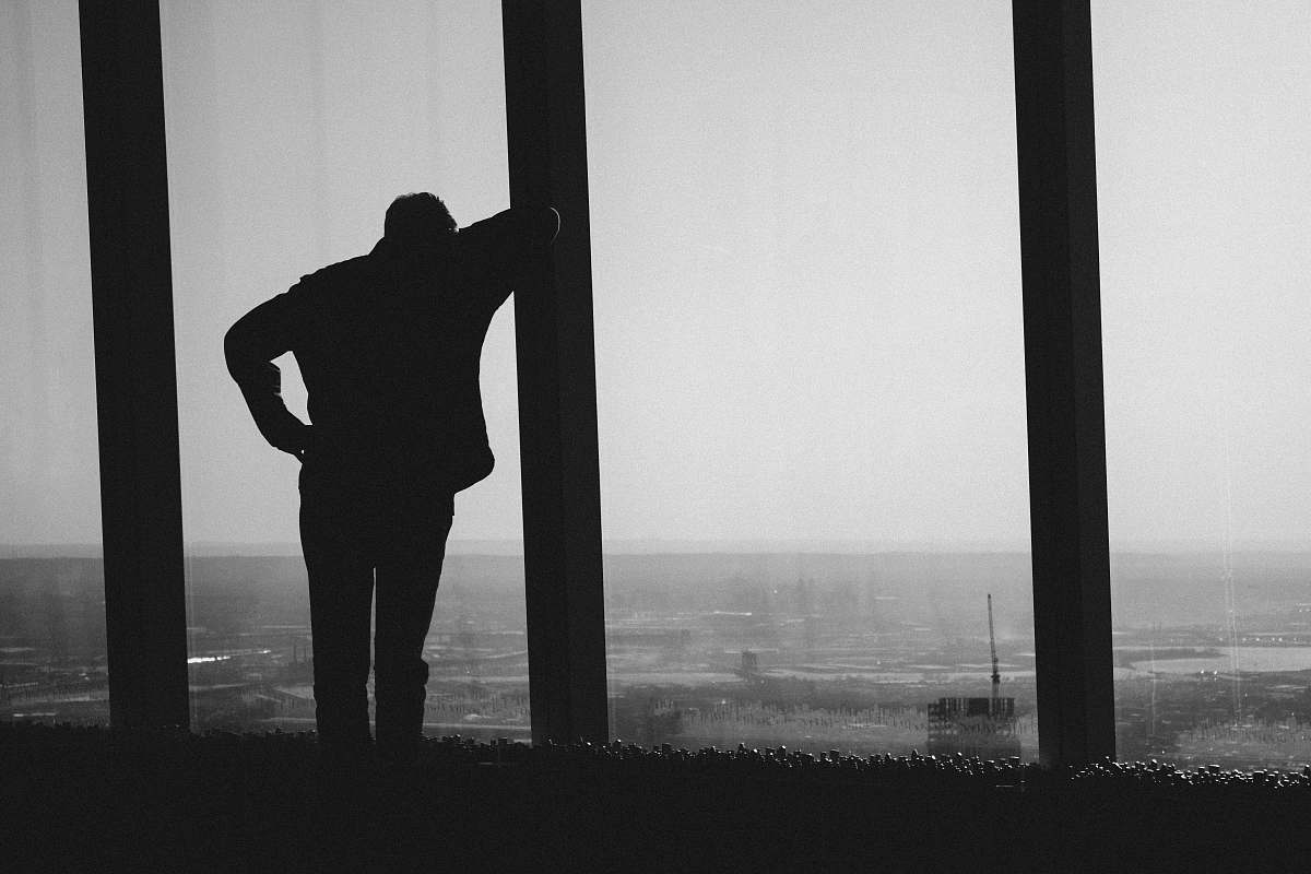 person silhouette photography of person leaning on post black-and-white