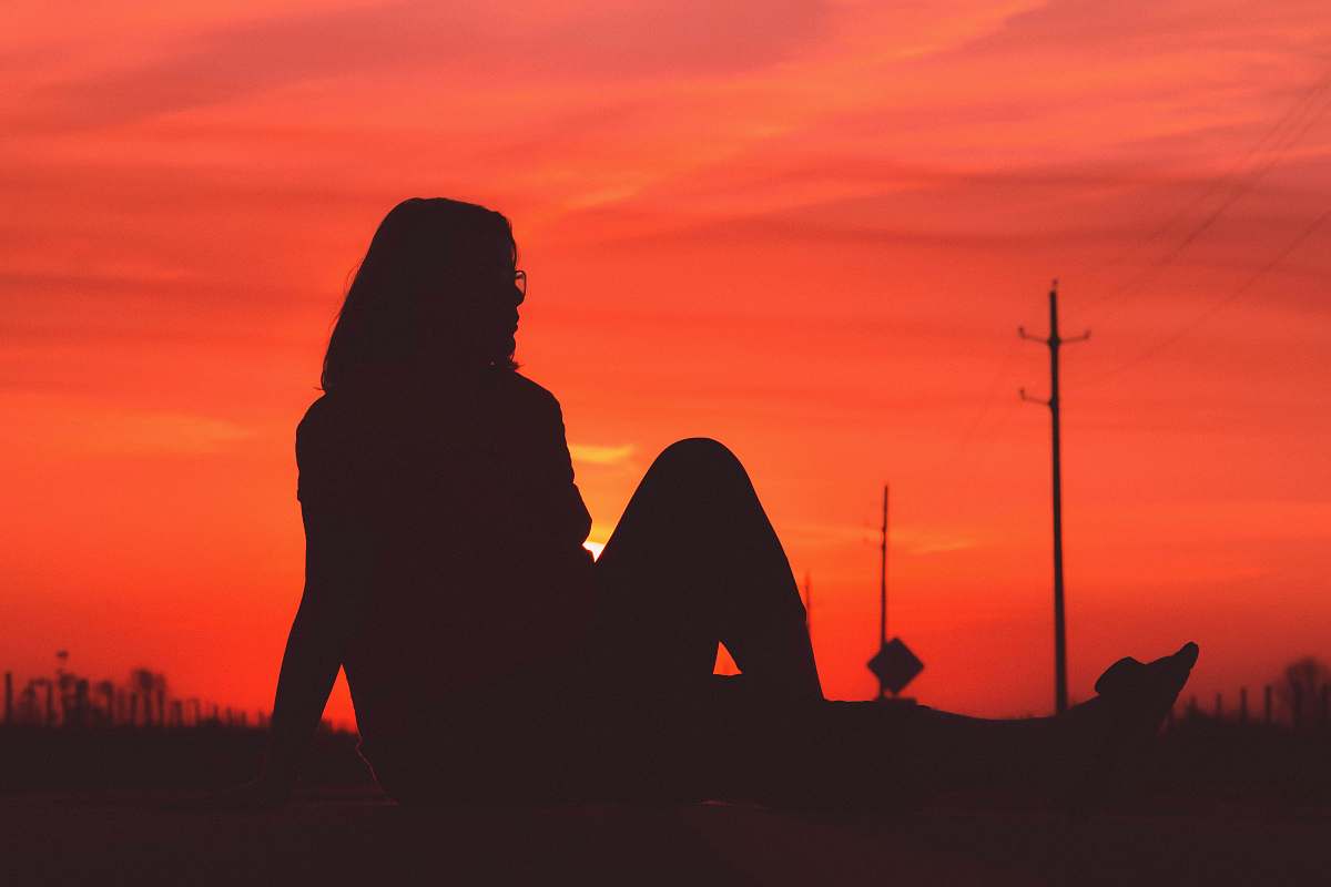 nature silhouette photography of person sitting on grass outdoors