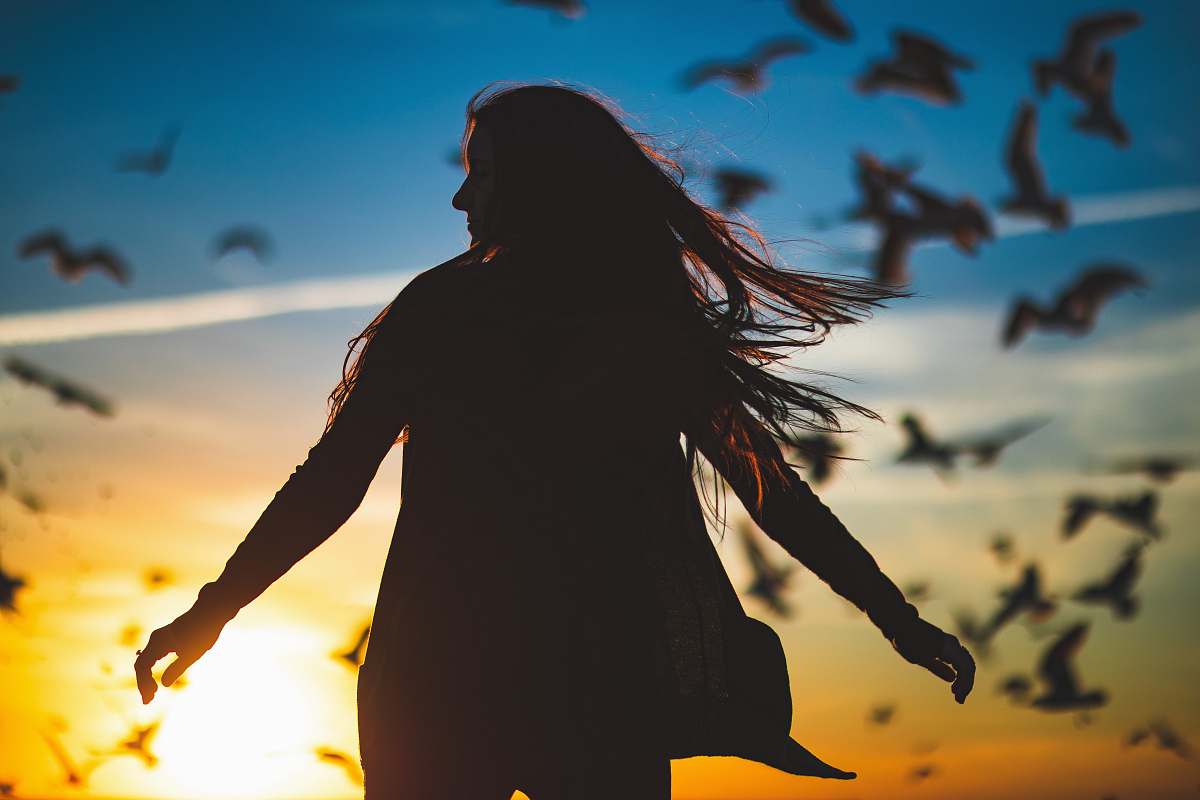 person silhouette photography of woman spreading her hands in front of flight of birds human