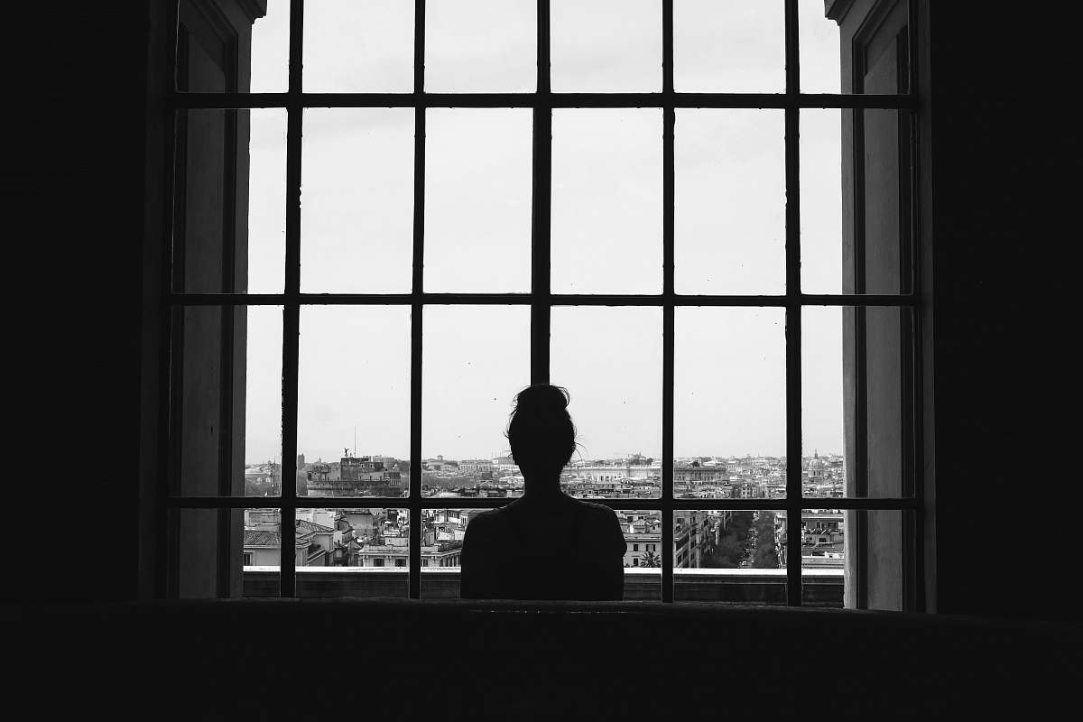 person woman standing in front glass window black-and-white