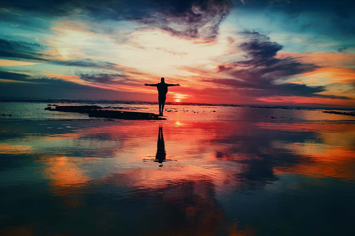 sunset silhouette of person standing on rock surrounded by body of water sunrise
