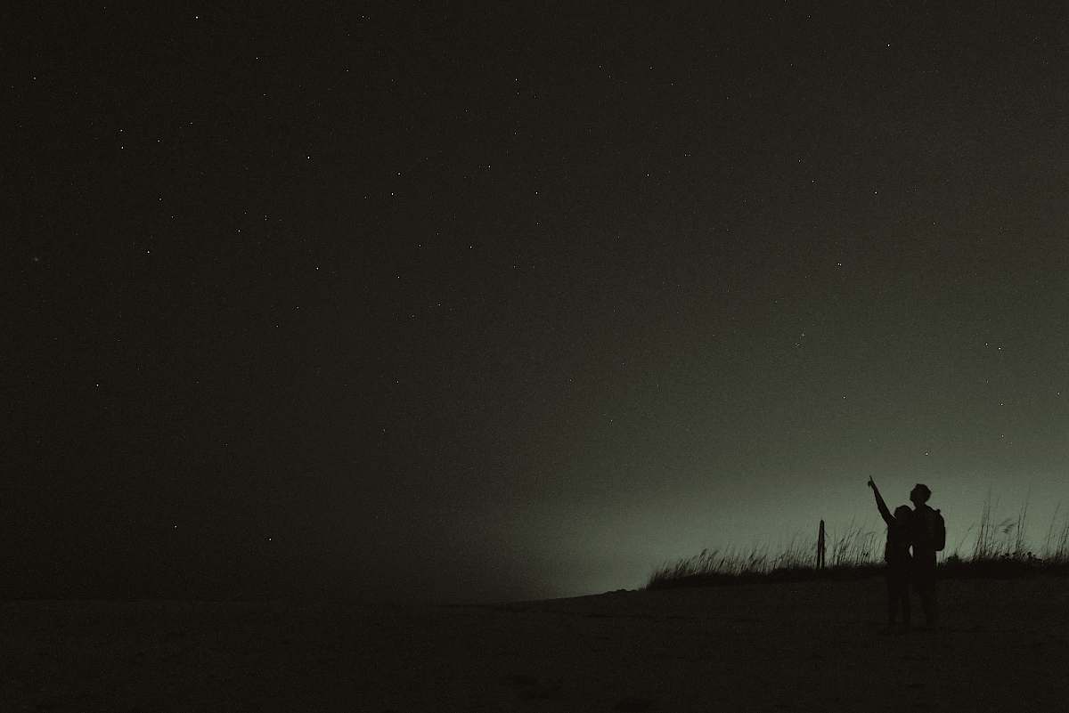black silhouette of two people looking at stars night sky