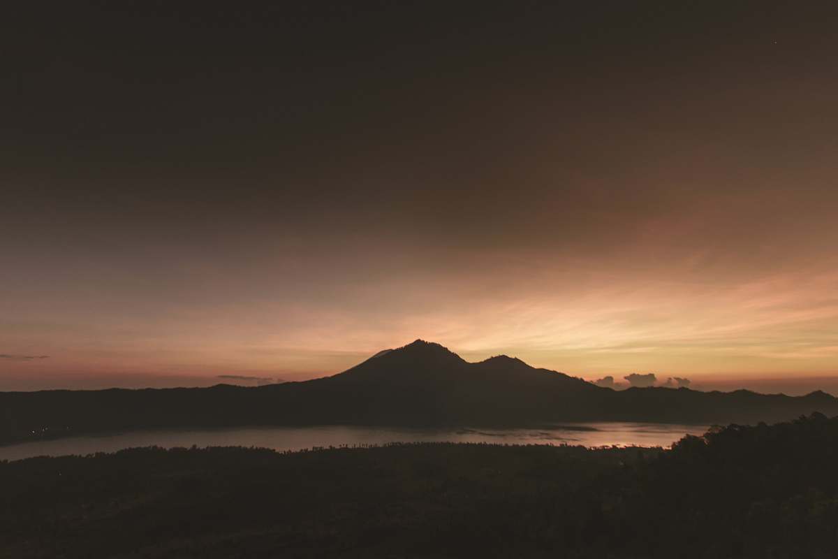 sunrise silhouette of mountain near body of water under brown clouds lake