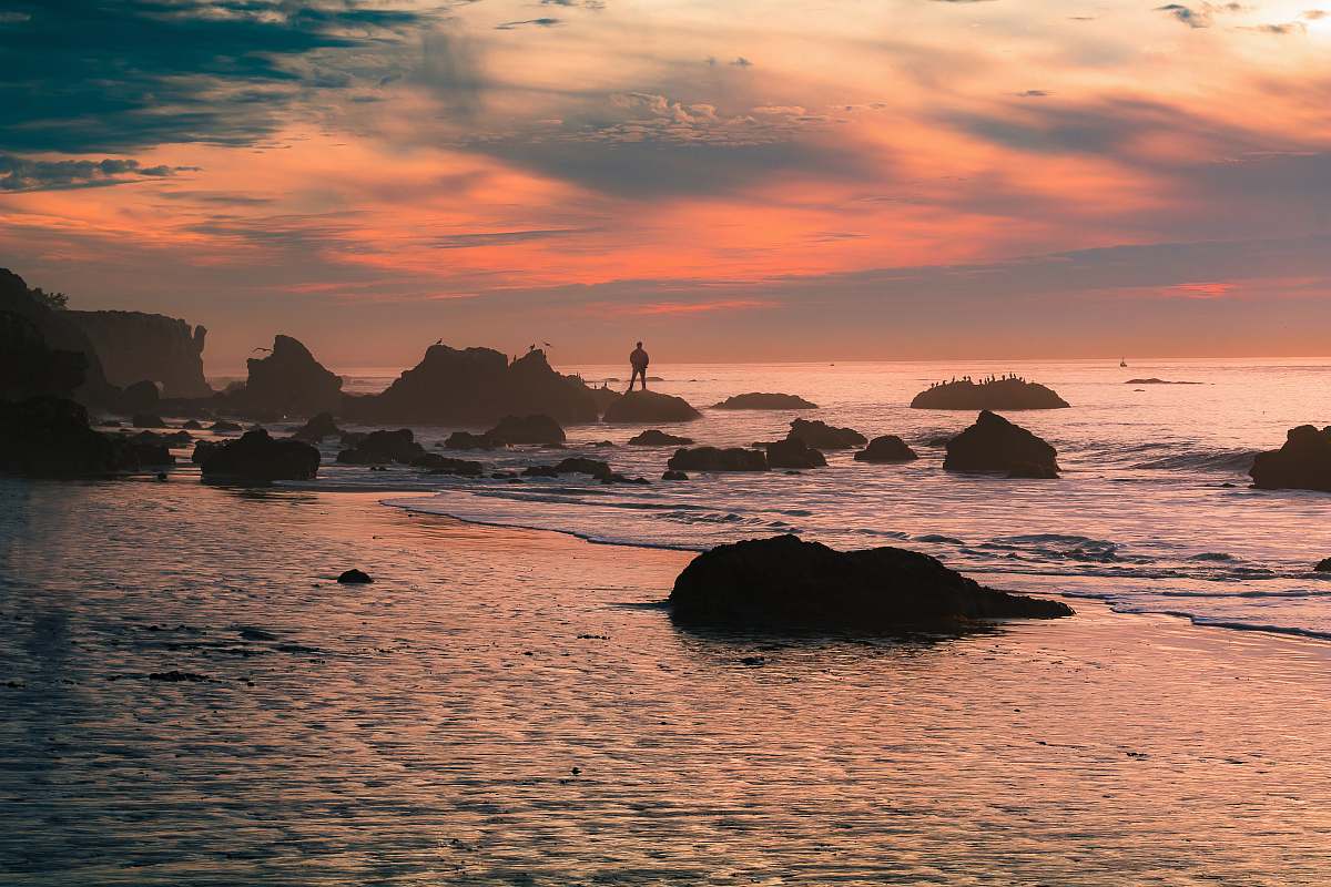 sky silhouette person standing on seashore rock during daytime sunrise