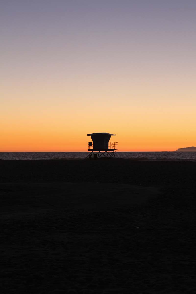 sunrise silhouette photo of shed on sand near sea during golden hours dawn