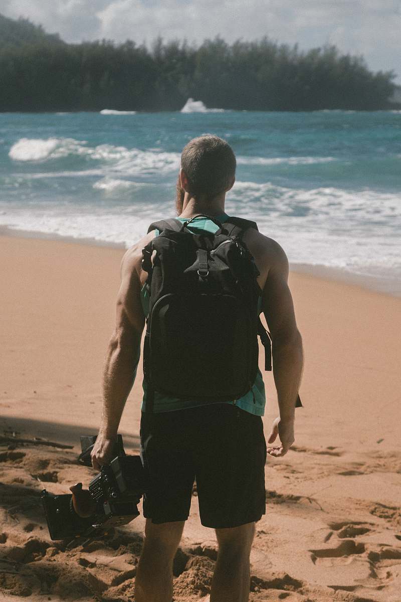 ocean man carrying video camera standing on beach sand facing sea sea