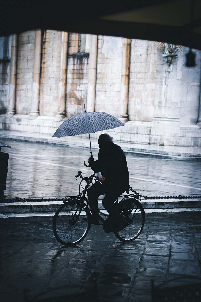 bike man riding bicycle while holding umbrella near street cyclist