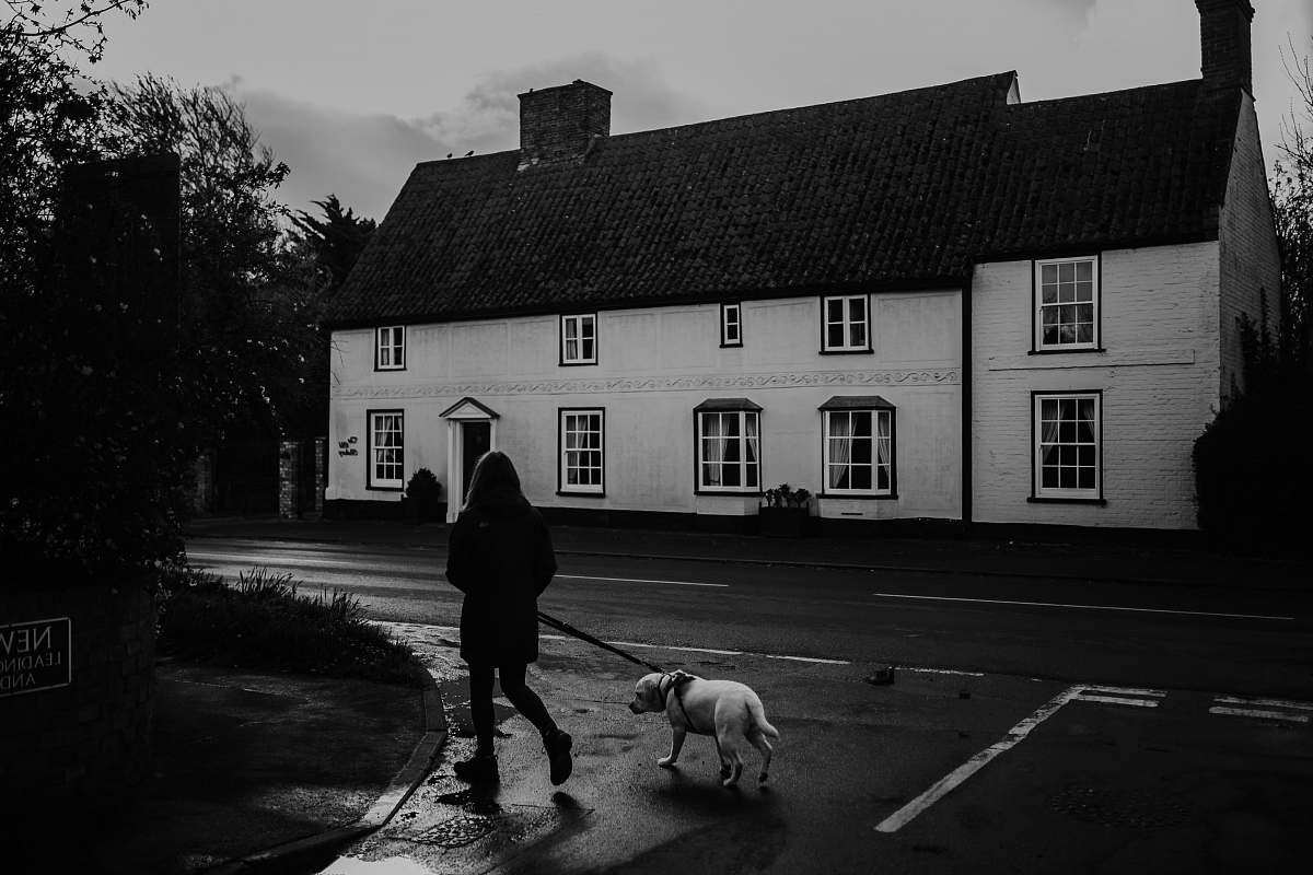 human grayscale photo of woman and dog walking near street and building people