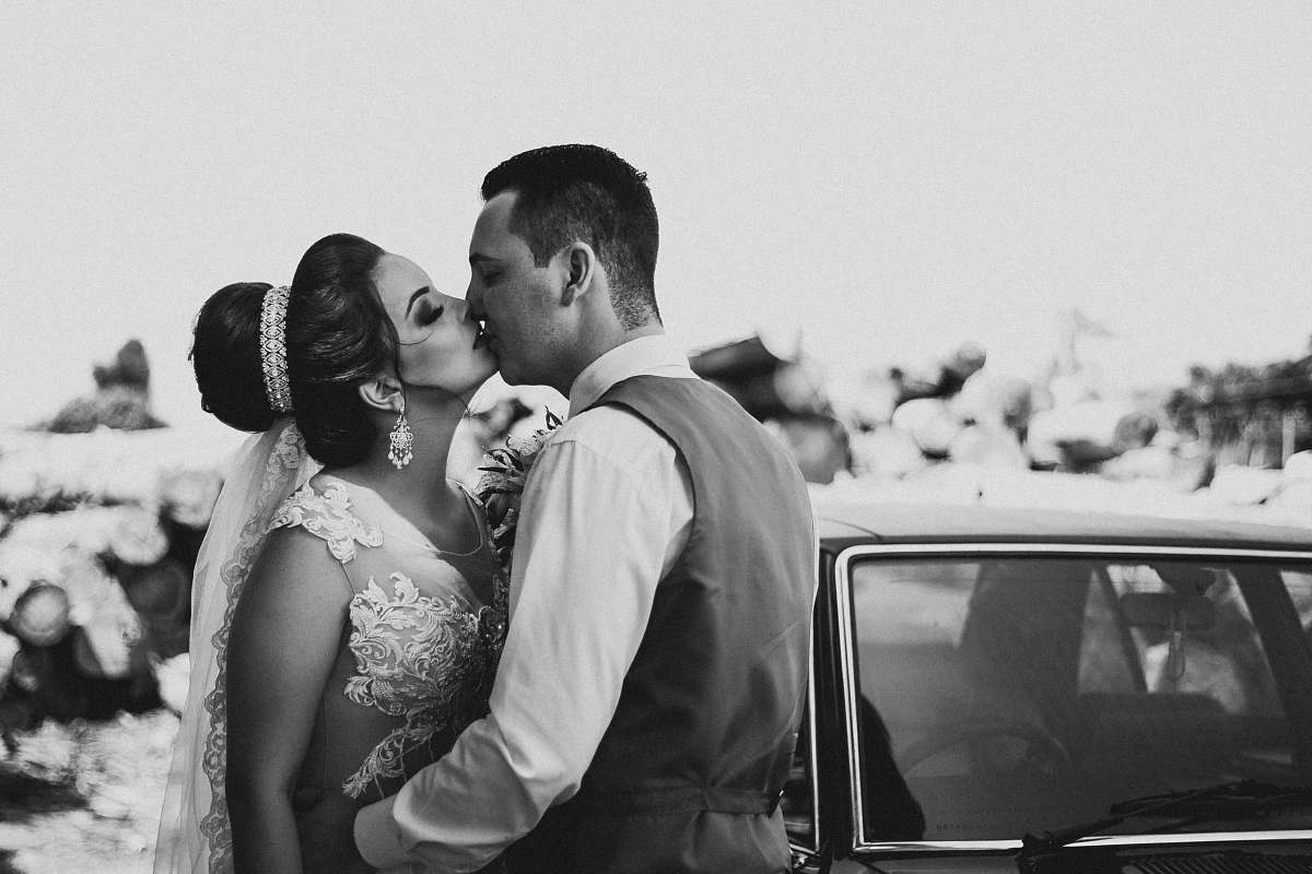 kissing grayscale photography of bride and groom kissing beside vehicle during daytime kiss