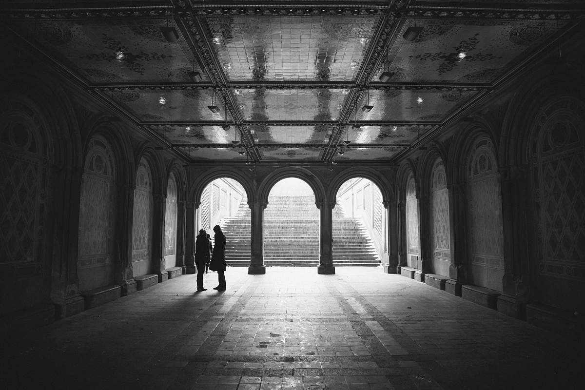 building grayscale two people standing on hallway arch