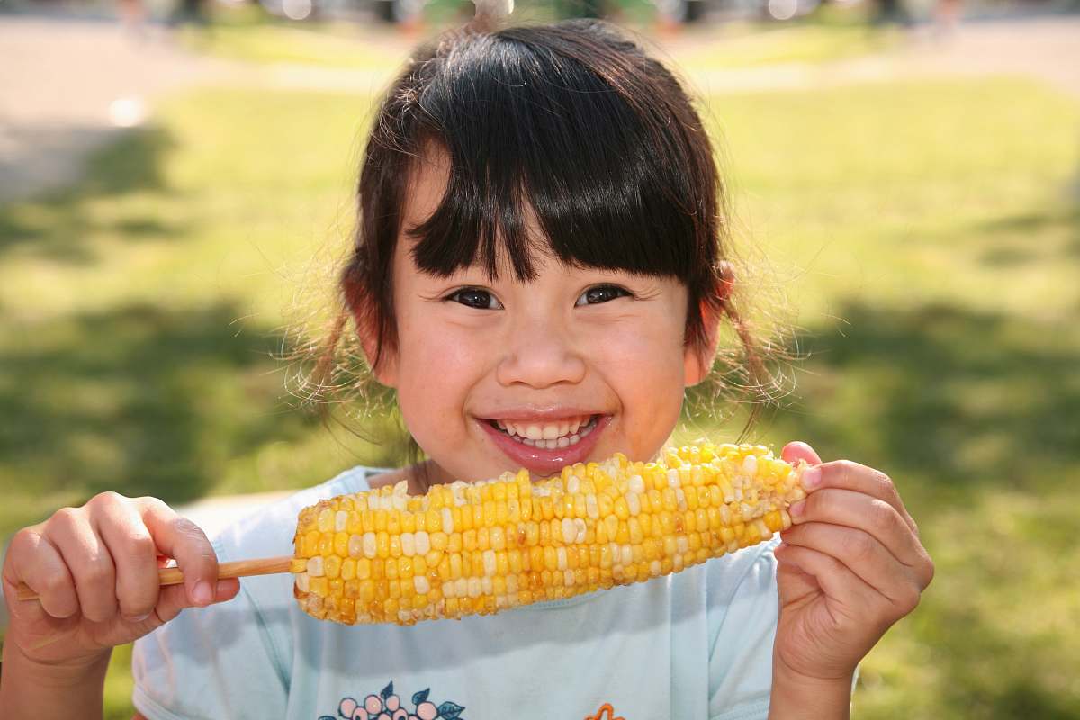 grain smiling girl holding cooked corn during daytime plant