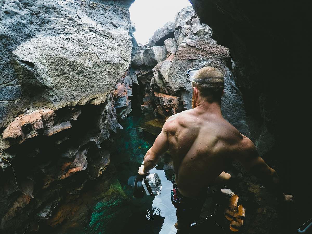 person black wearing black shorts near body of water between road formation during daytime cave