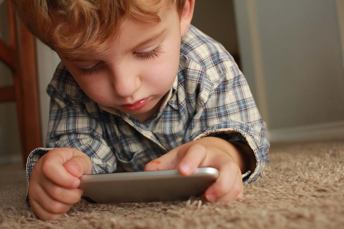 people boy holding smartphone while lying on rug person