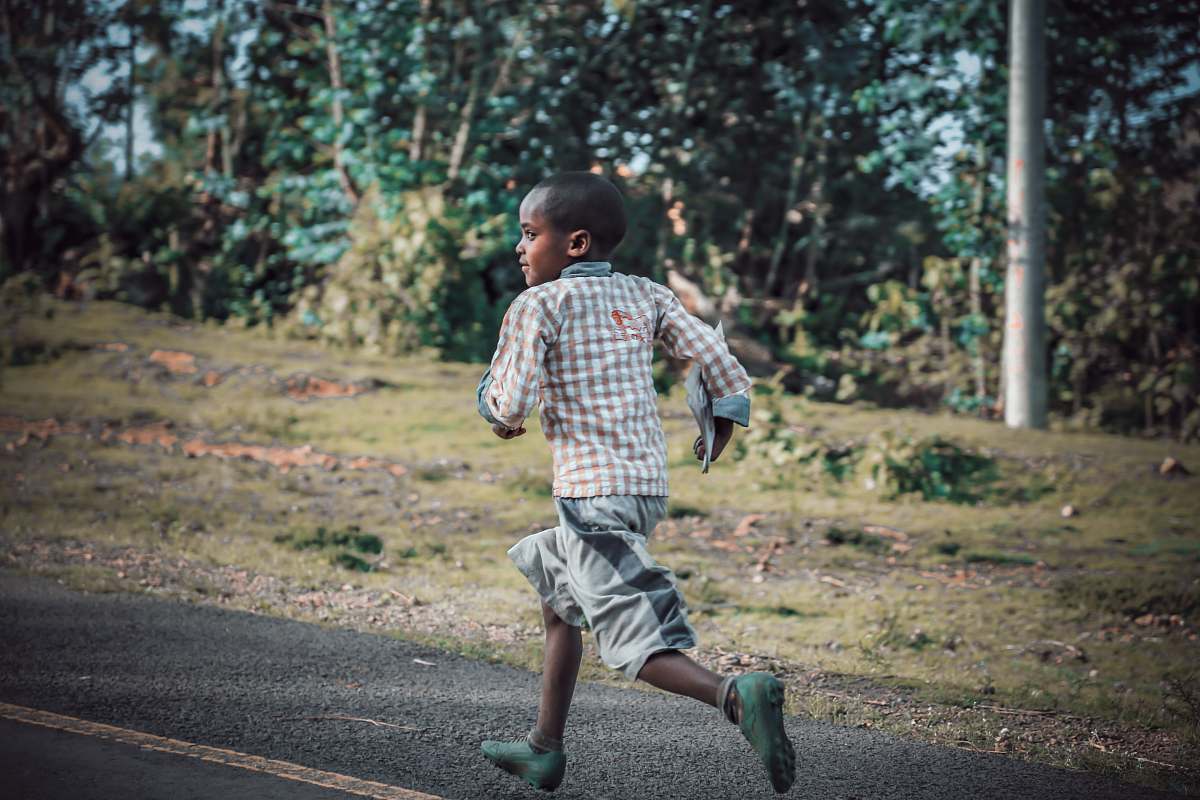 person boy running on asphalt road near grass field people