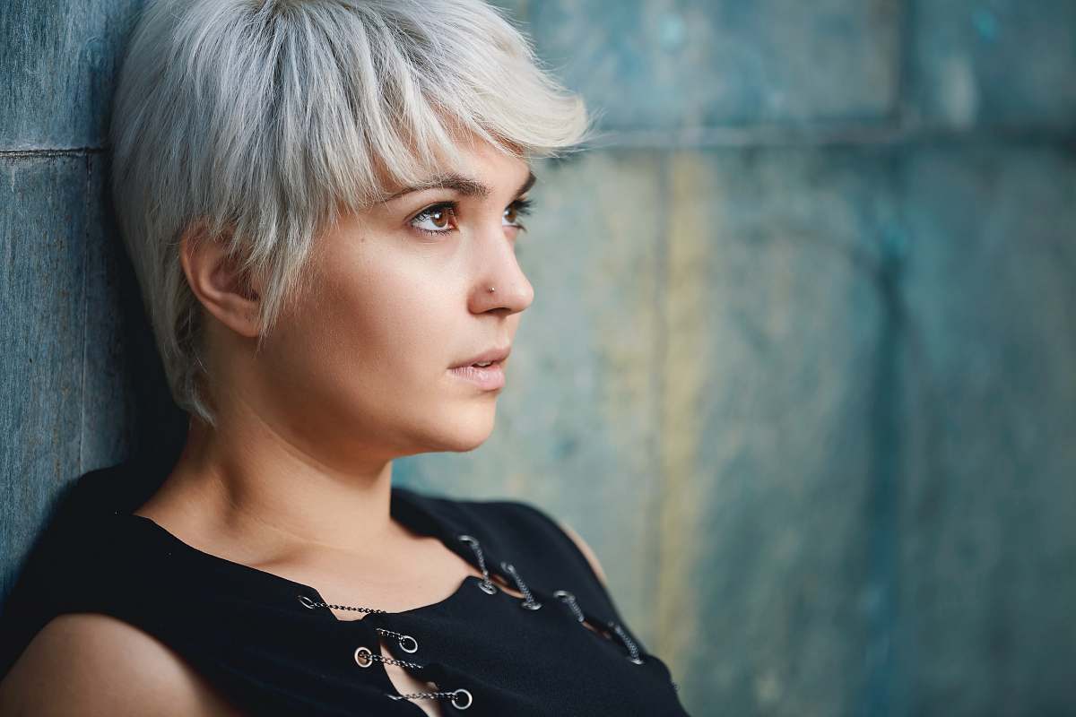 person close up photography of woman wearing black sleeveless top leaning on gray concrete wall people