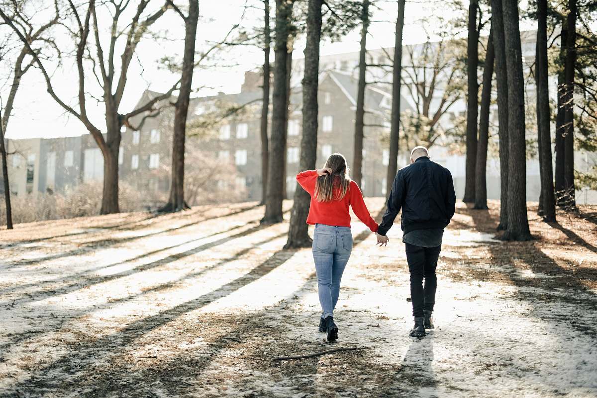 people couple holding hands while walking near brown trees during daytime person