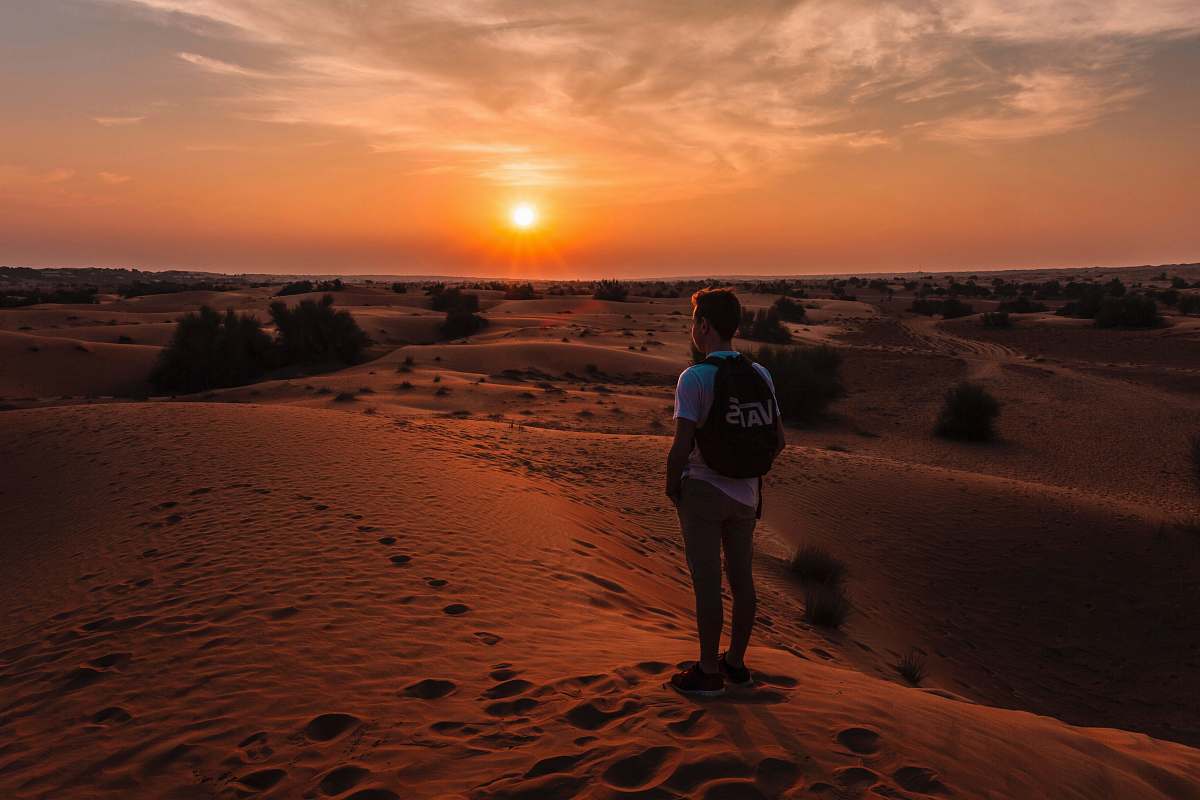person golden hour photography of man standing on top of a hill people