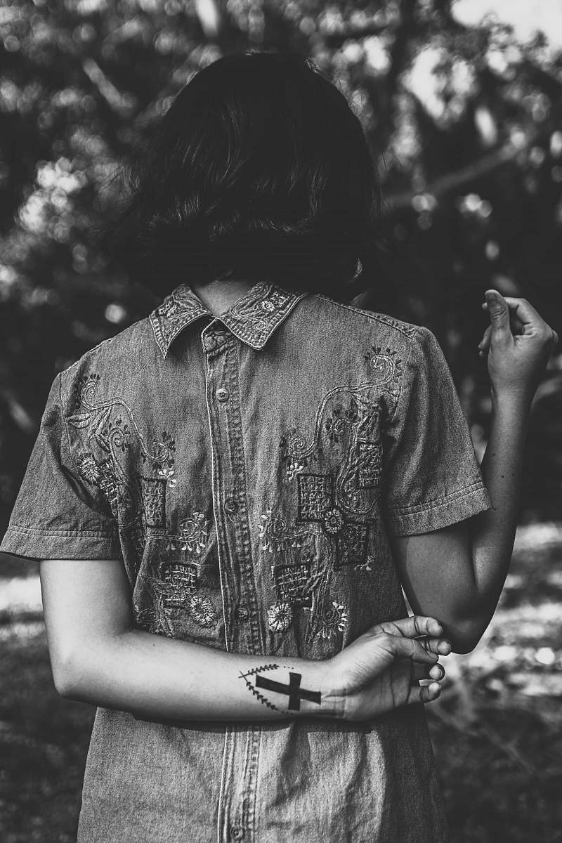 person gray scale photo of a woman standing in front of bushes black-and-white