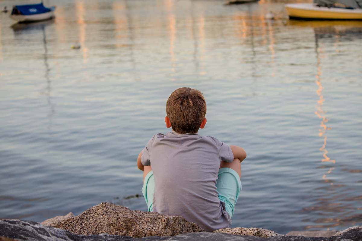 people gray sitting on gray concrete pavement facing ocean water during daytime person