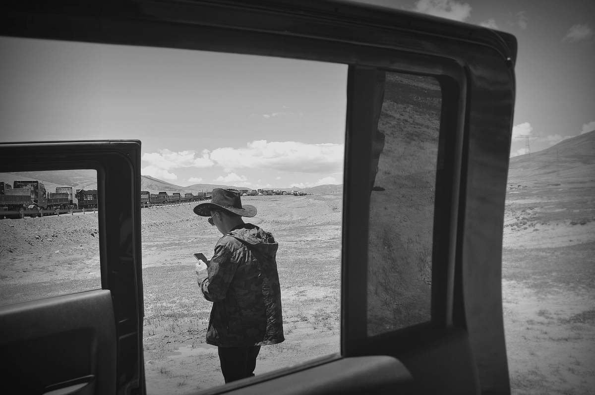 people grayscale photo of man holding smartphone through vahicle window black-and-white