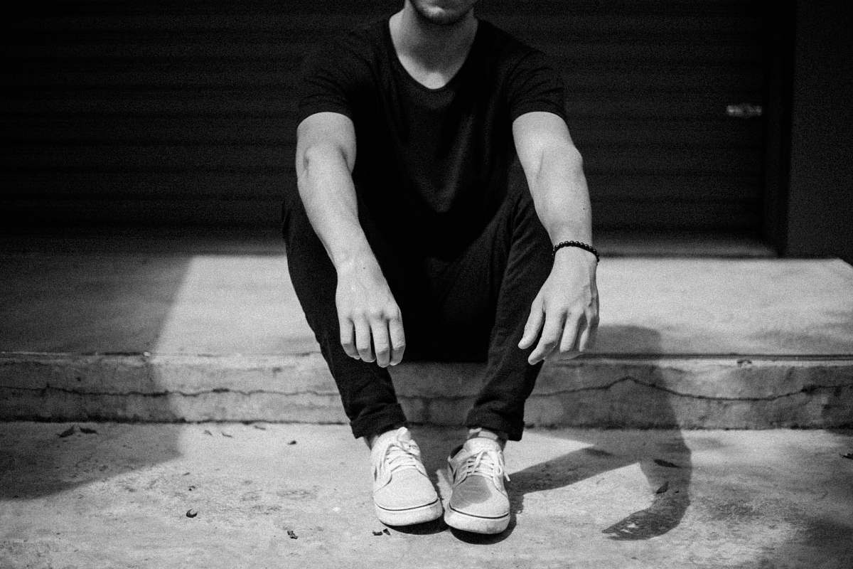 people grayscale photo of man sitting on doorway black-and-white