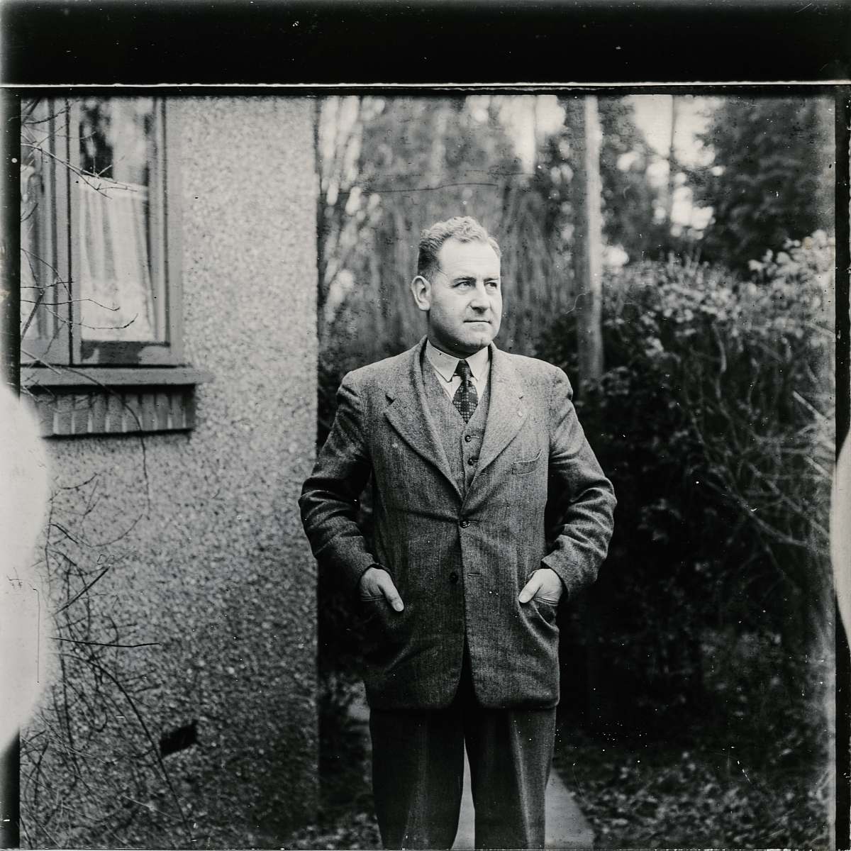 people grayscale photo of man wearing suit standing beside wall with mirror black-and-white