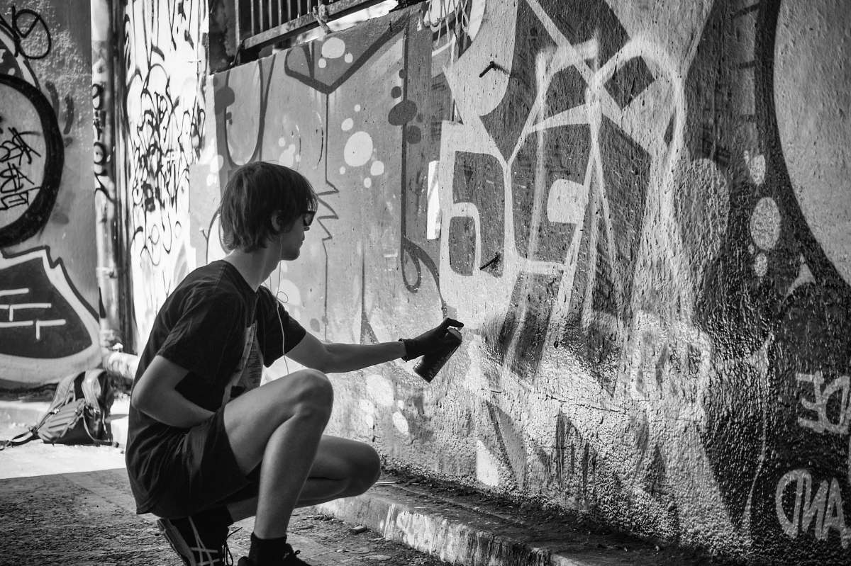 people grayscale photography of man vandalize the wall during daytime black-and-white