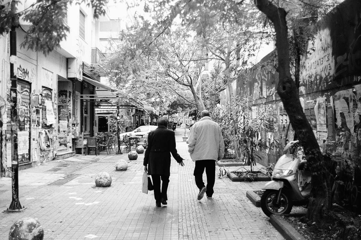 people grayscale photography of two people walking on hallway beside motor scooter black-and-white