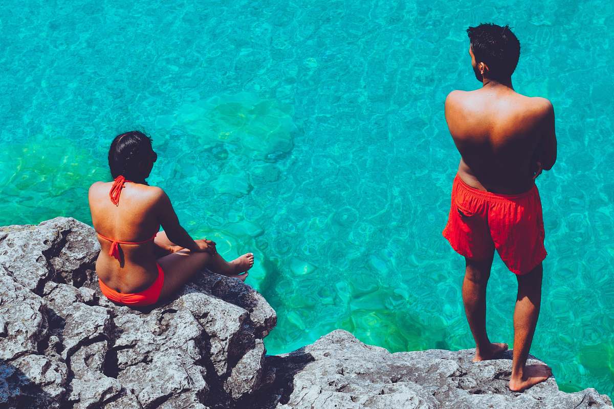 person man and woman sitting on boulder near body of water people