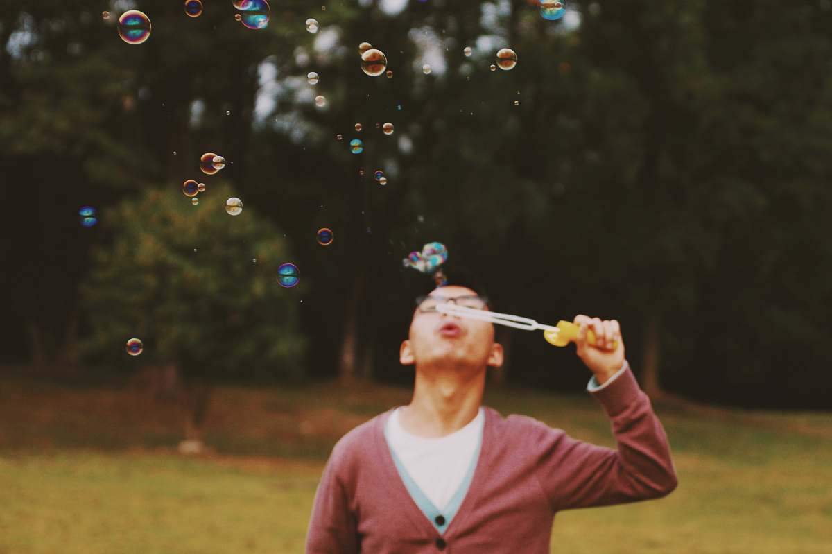 people man holding bubble stick near green trees person